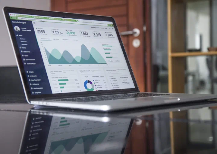 A laptop on a dark desk displaying a dashboard with charts and summary panels