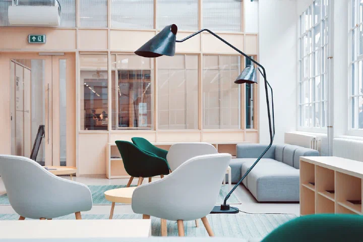 A bright open-plan office lounge with meeting seating and shelving, representing shared bookable spaces