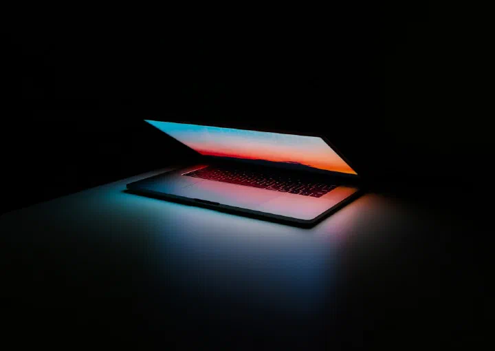 A dimly lit laptop glowing on a dark desk