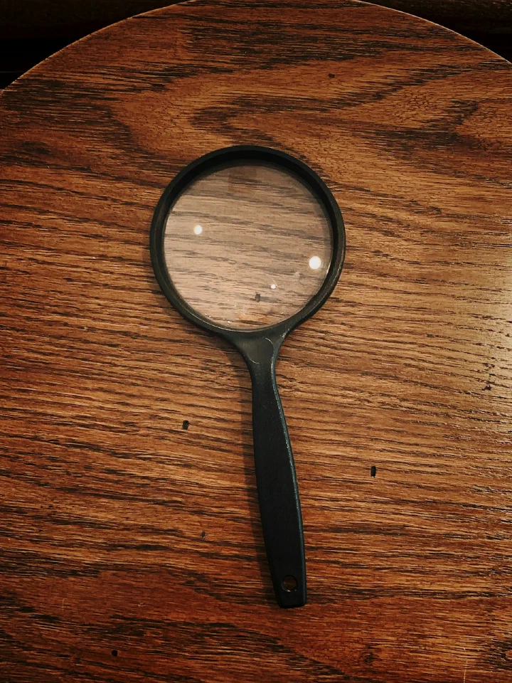 A magnifying glass resting on a wooden table, framing a section of the wood grain