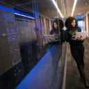 An IT professional reviewing equipment on a laptop in a server room