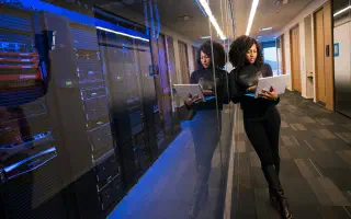 An IT professional reviewing equipment on a laptop in a server room